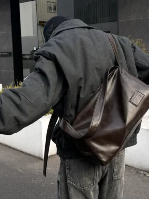 Brown soft PU leather crossbody sling bag worn with a dark gray workwear jacket and jeans in an urban streetwear setting