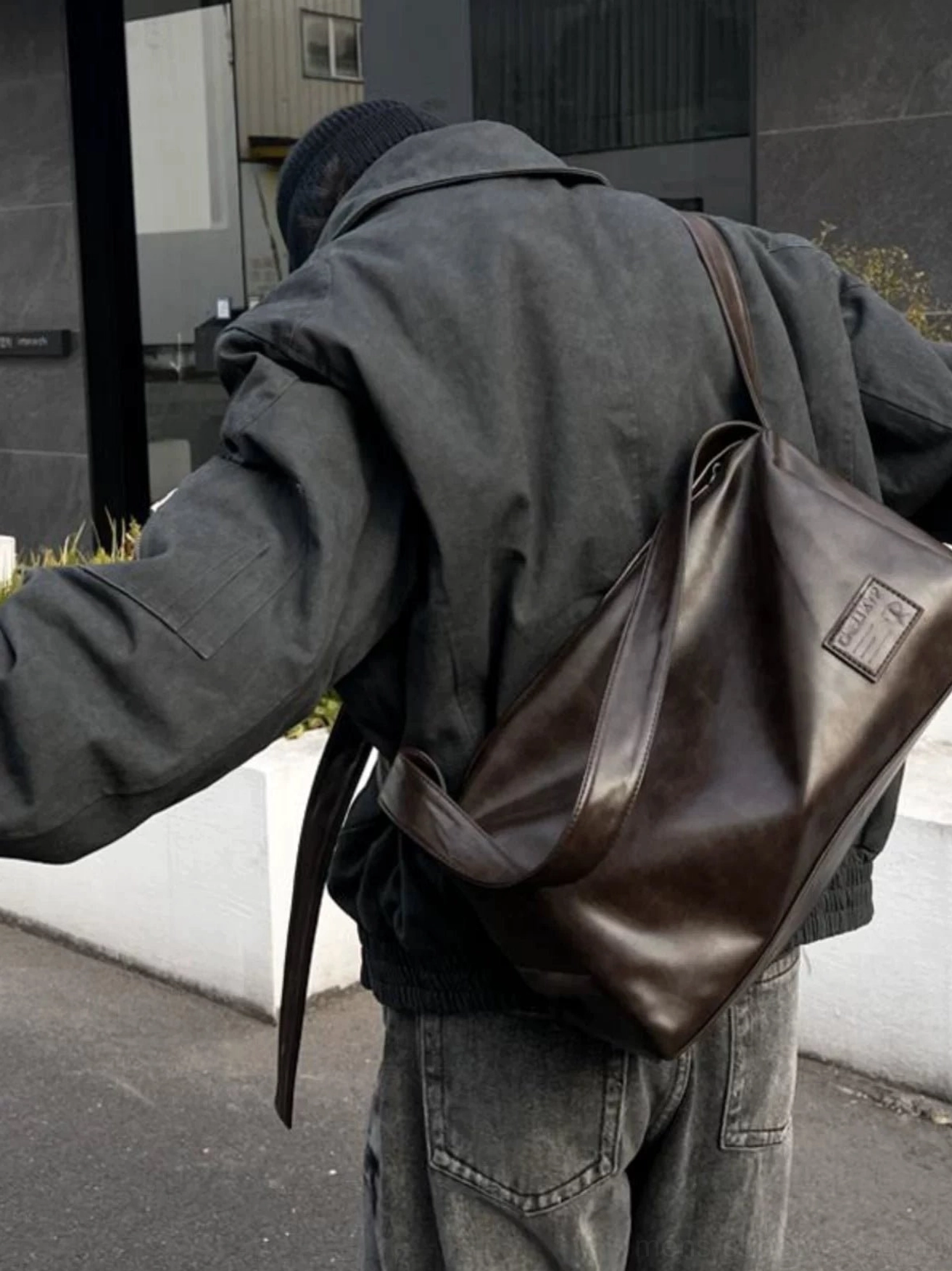Brown soft PU leather crossbody sling bag worn with a dark gray workwear jacket and jeans in an urban streetwear setting