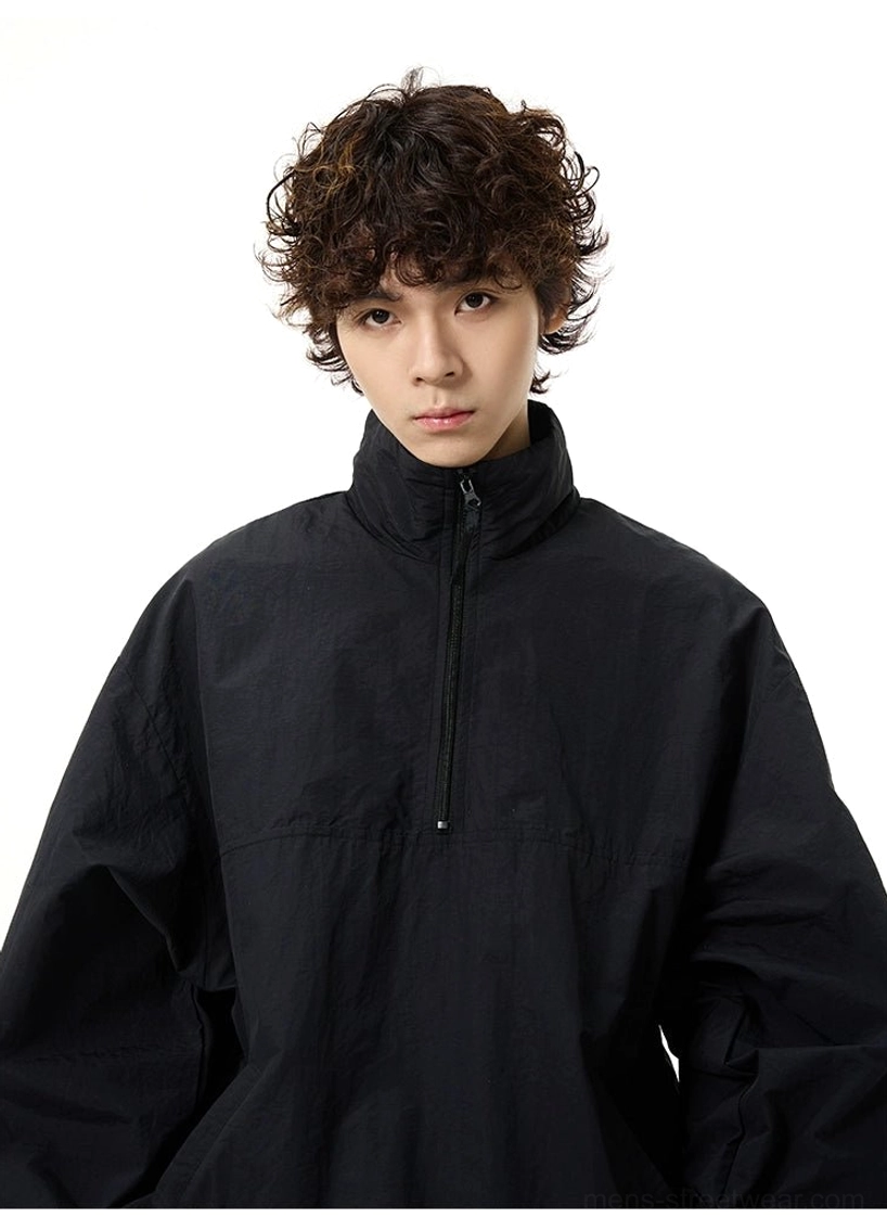Close-up front view of an oversized solid black half-zip windbreaker with stand collar and relaxed sleeves