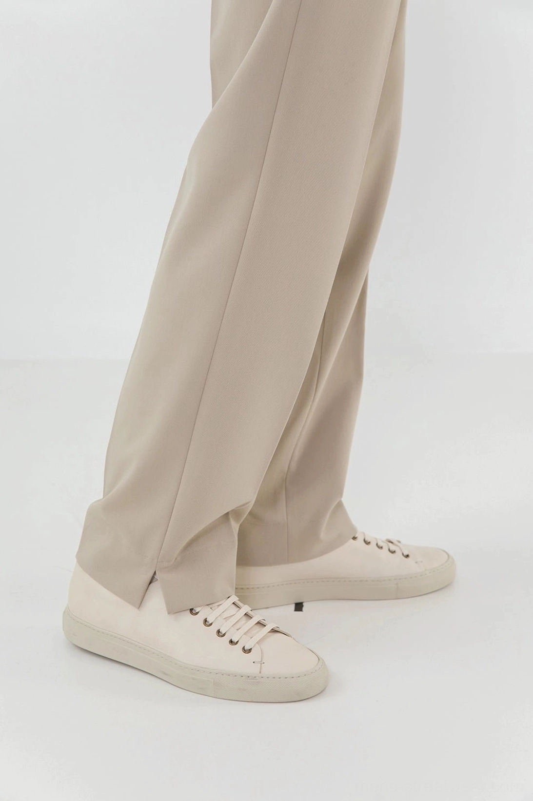 Ankle split hem detail close-up beige pants white low-top casual sneakers studio background