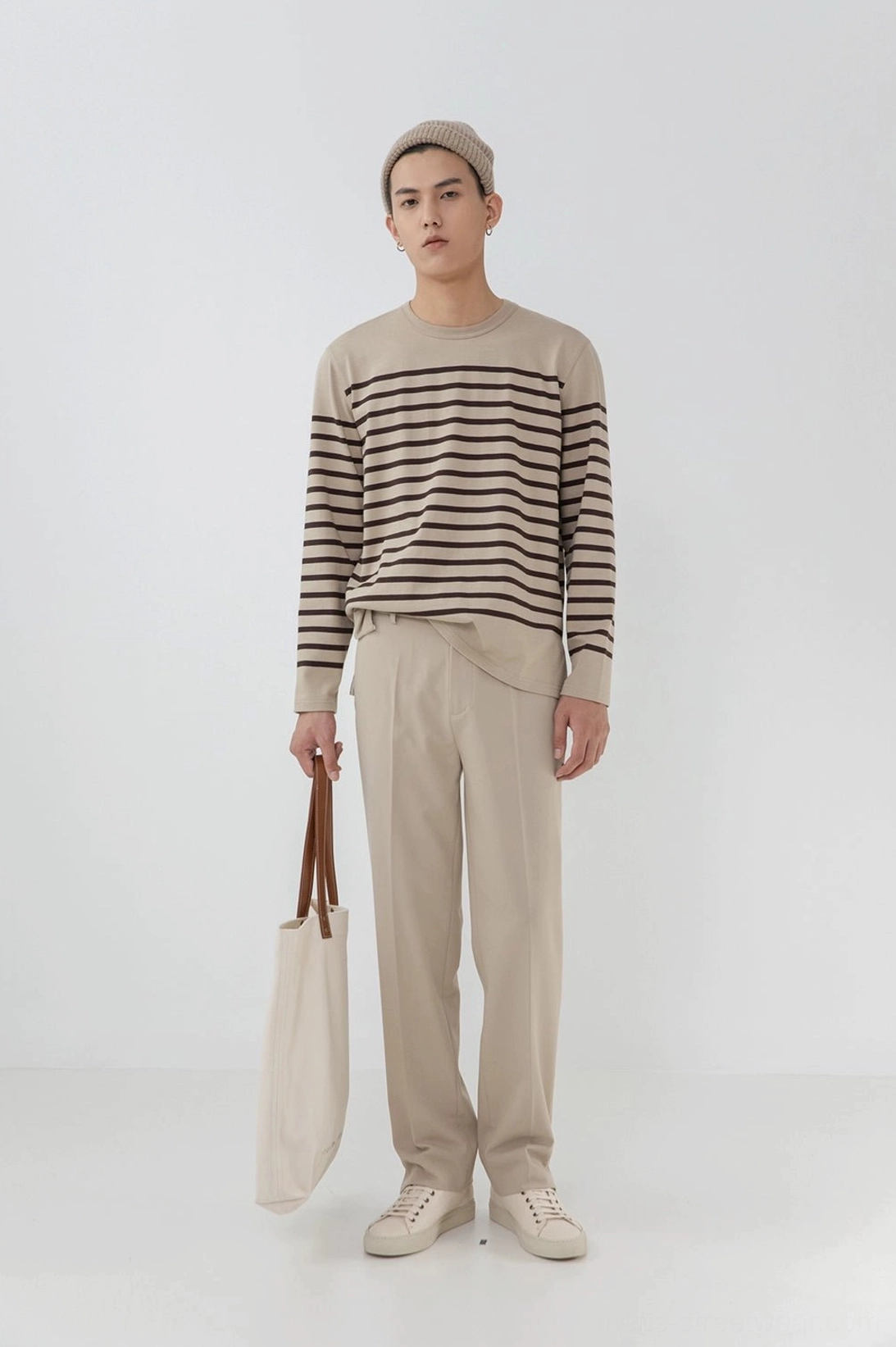 Full body front view male model beige split hem pants striped knit beanie canvas tote warm neutrals