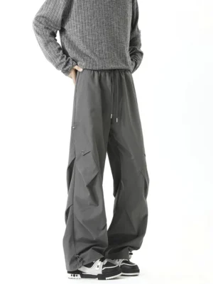 Dark gray wide-leg cargo pants on a male model with elastic drawstring waist, utility side pockets, relaxed pleats, and adjustable hems