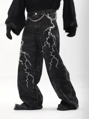 Left three-quarter view of black acid-washed lightning print wide-leg denim trousers with silver waist chain and loose streetwear silhouette