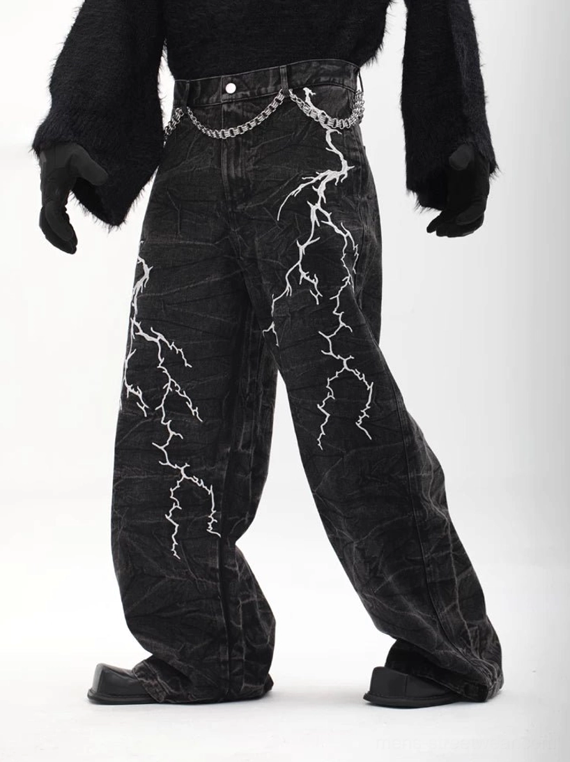 Left three-quarter view of black acid-washed lightning print wide-leg denim trousers with silver waist chain and loose streetwear silhouette