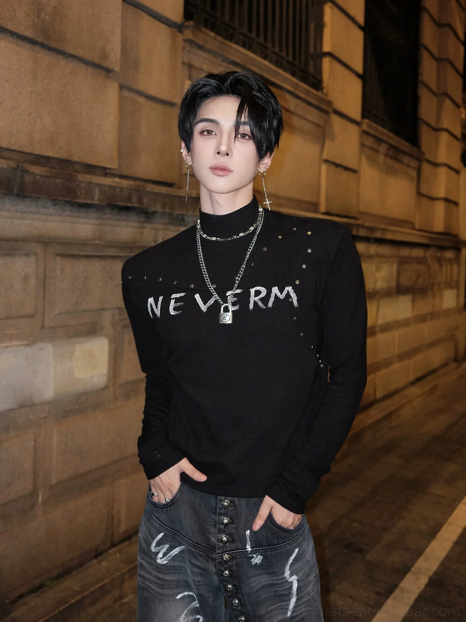 Three-quarter view of a slim studded gothic knit turtleneck sweater with distressed graphic print, shoulder studs, graphic denim, and layered silver necklaces
