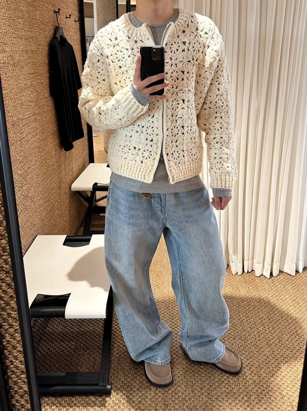 Sun-faded light blue wide leg denim jeans styled with a ribbed knit sweater, white sneakers, and bucket bag in a lobby