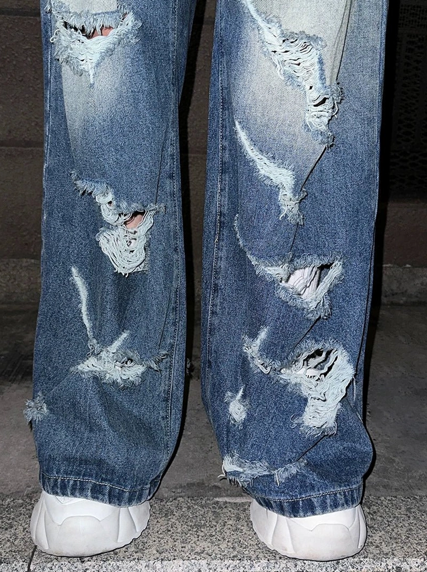 Close-up of frayed ripped lower legs on faded blue super distressed wide-leg jeans over white chunky sneakers