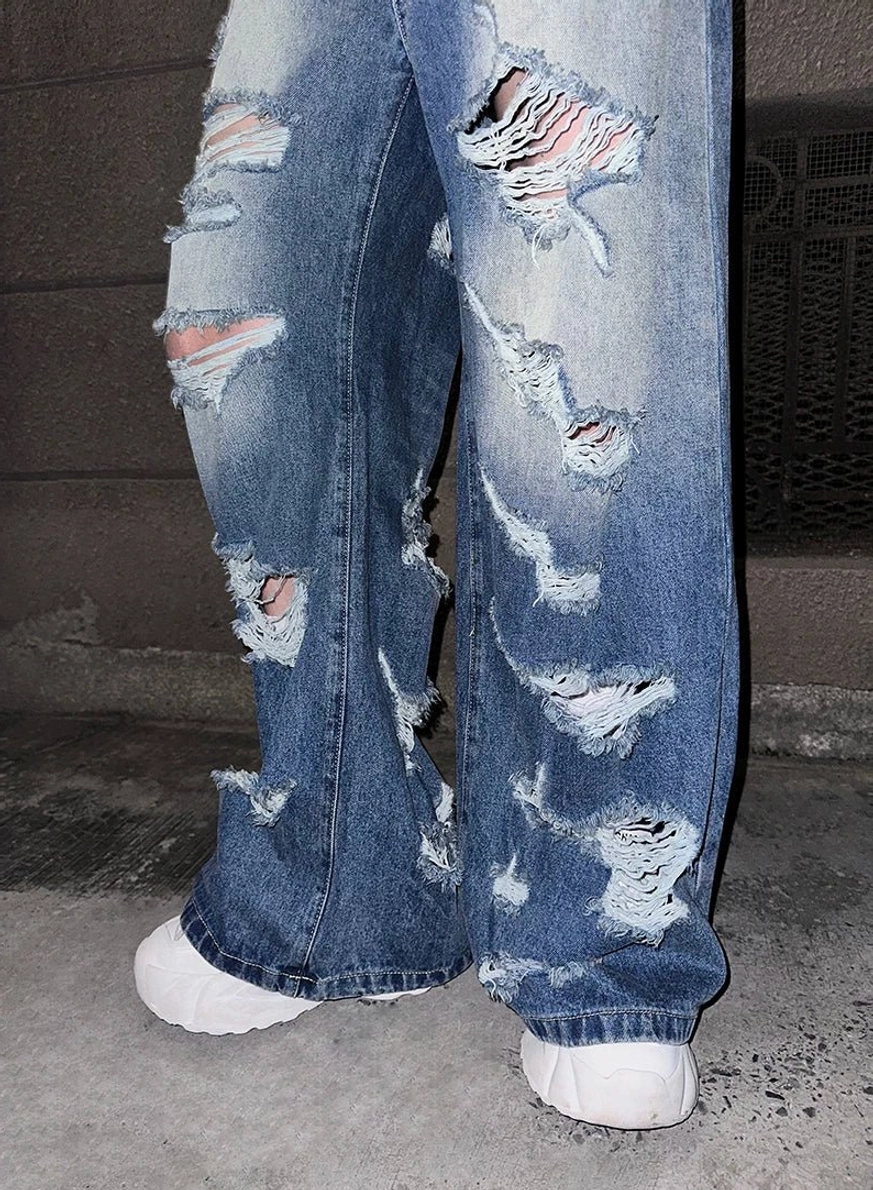Flat lay of super distressed wide-leg blue jeans with large irregular rips and white chunky sneaker styling