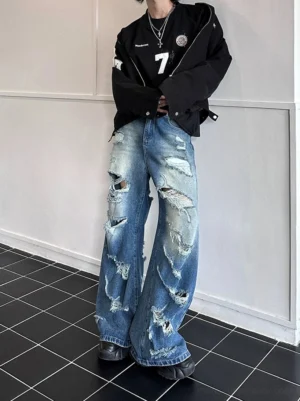 Front full-body view of super distressed wide-leg blue jeans styled with a black varsity jacket and chunky sneakers for Seoul streetwear