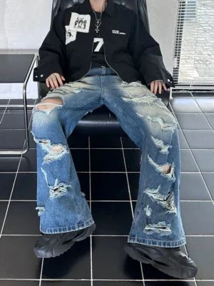 Low-angle seated view of faded blue wide-leg jeans with heavy ripped distressing and raw frayed details