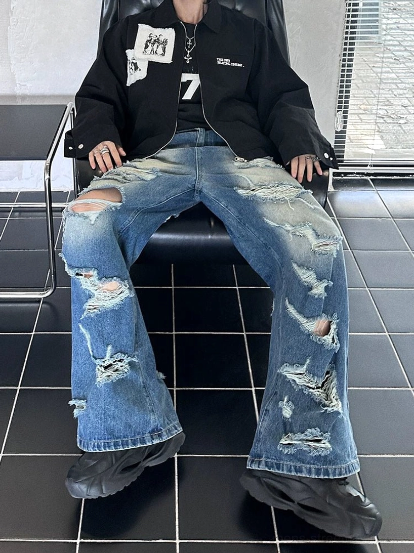 Low-angle seated view of faded blue wide-leg jeans with heavy ripped distressing and raw frayed details
