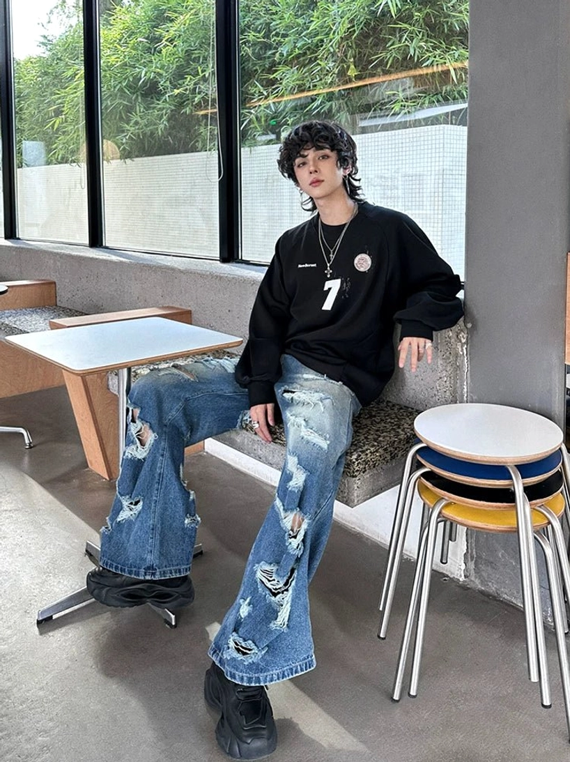 Side seated view of heavily ripped faded blue wide-leg jeans styled with black leather shoes in Korean streetwear fashion