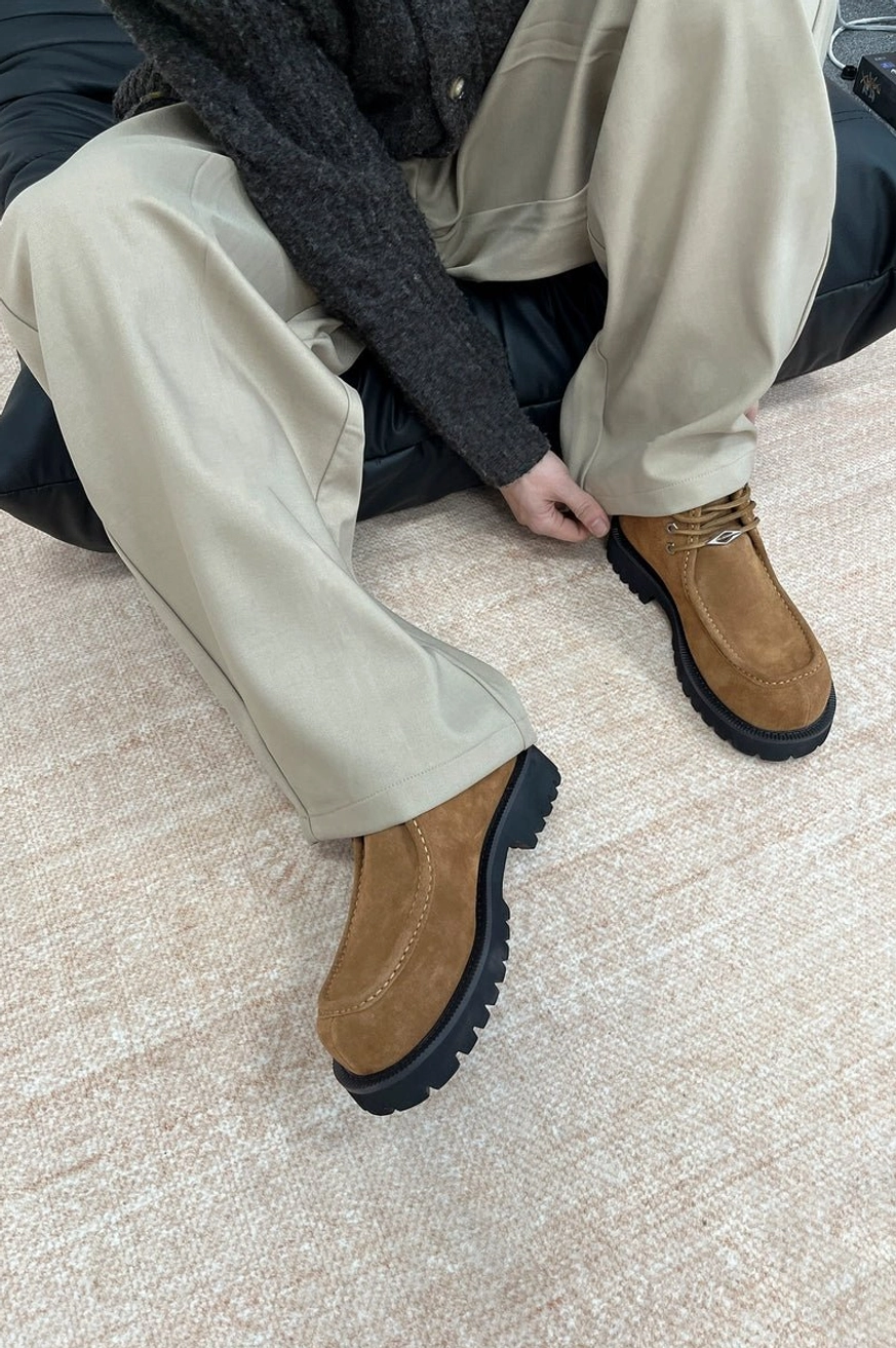 Tan brown shearling moc toe lug boots worn with khaki pants and dark knitwear for relaxed winter streetwear styling