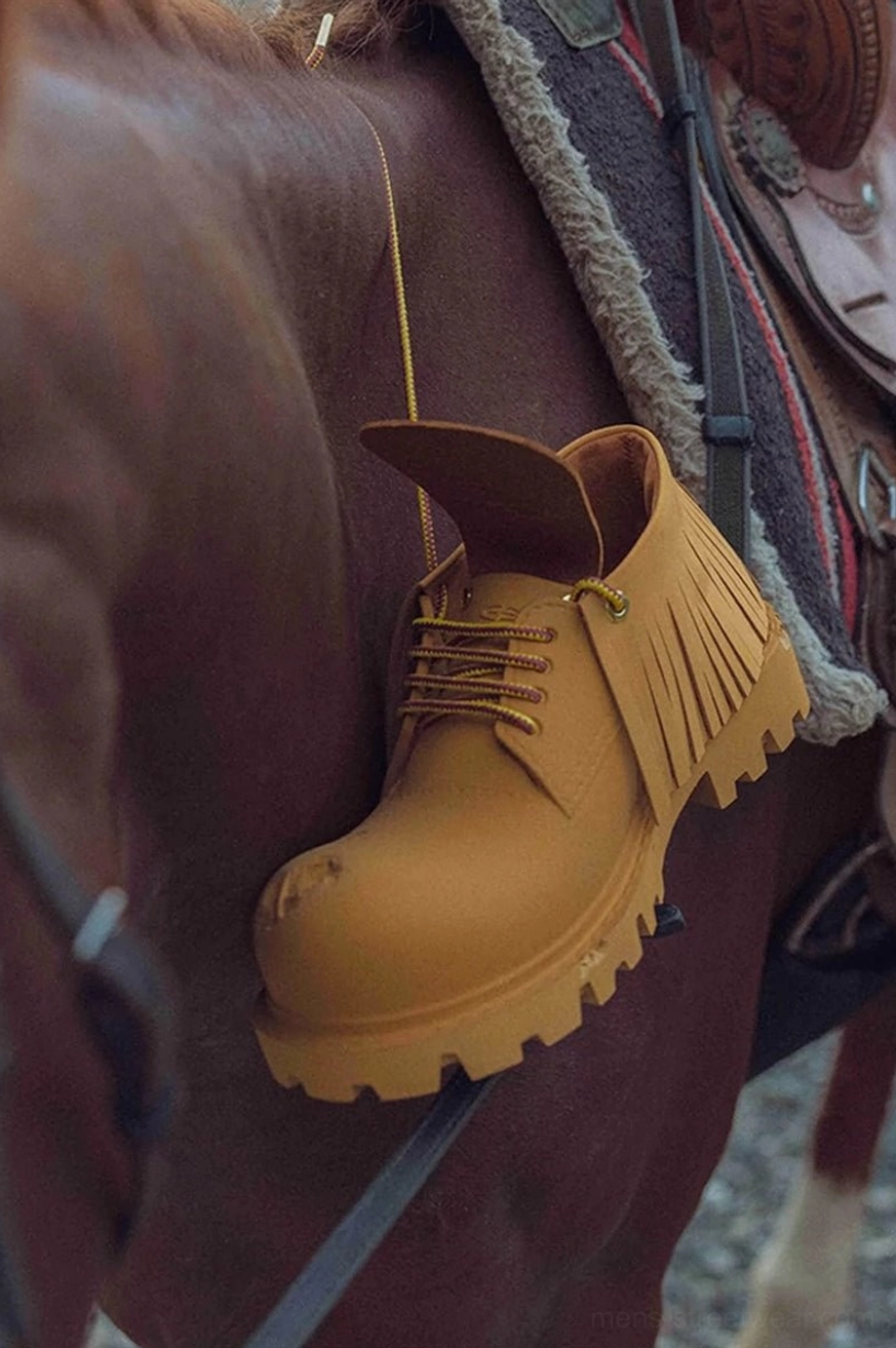Close-up side view of tan fringe platform derby shoe hanging on an equestrian saddle with visible fringe and chunky lug outsole