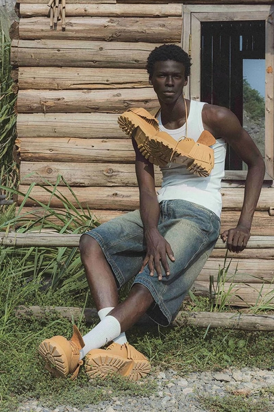 Male model wearing tan fringe platform derby shoes with white socks and denim shorts in a casual Western outdoor outfit