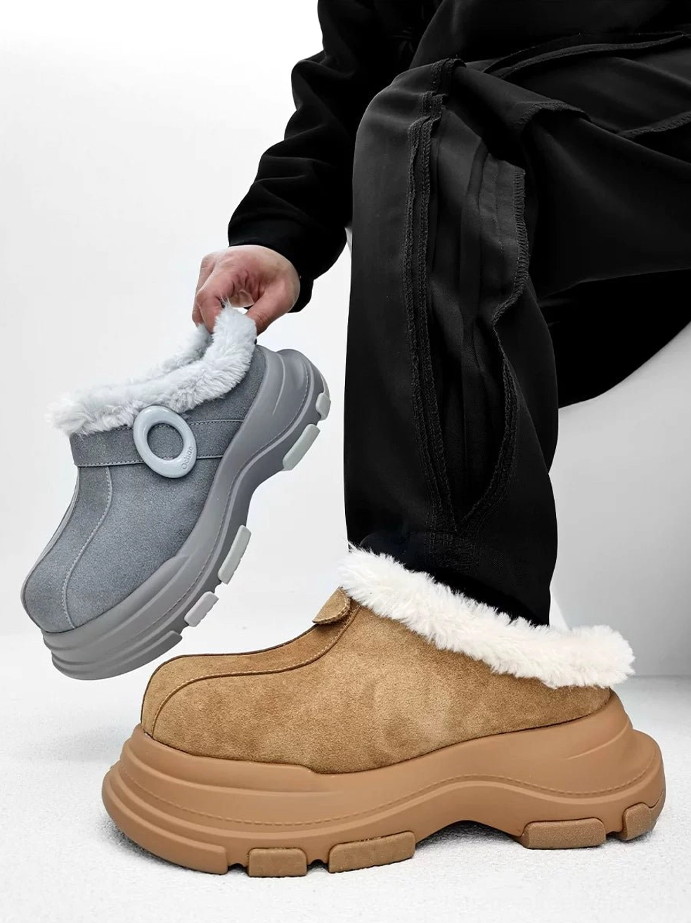 Tan and gray fleece-lined platform clogs displayed from the front with chunky rubber soles, fluffy fur trim, and circular strap details