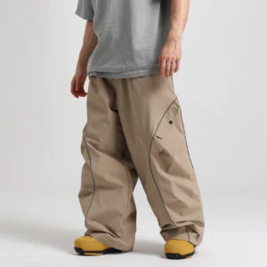 Tan khaki reflective wide-leg snow pants with dark contrast piping, oversized techwear silhouette, utility pockets, and yellow snow boots