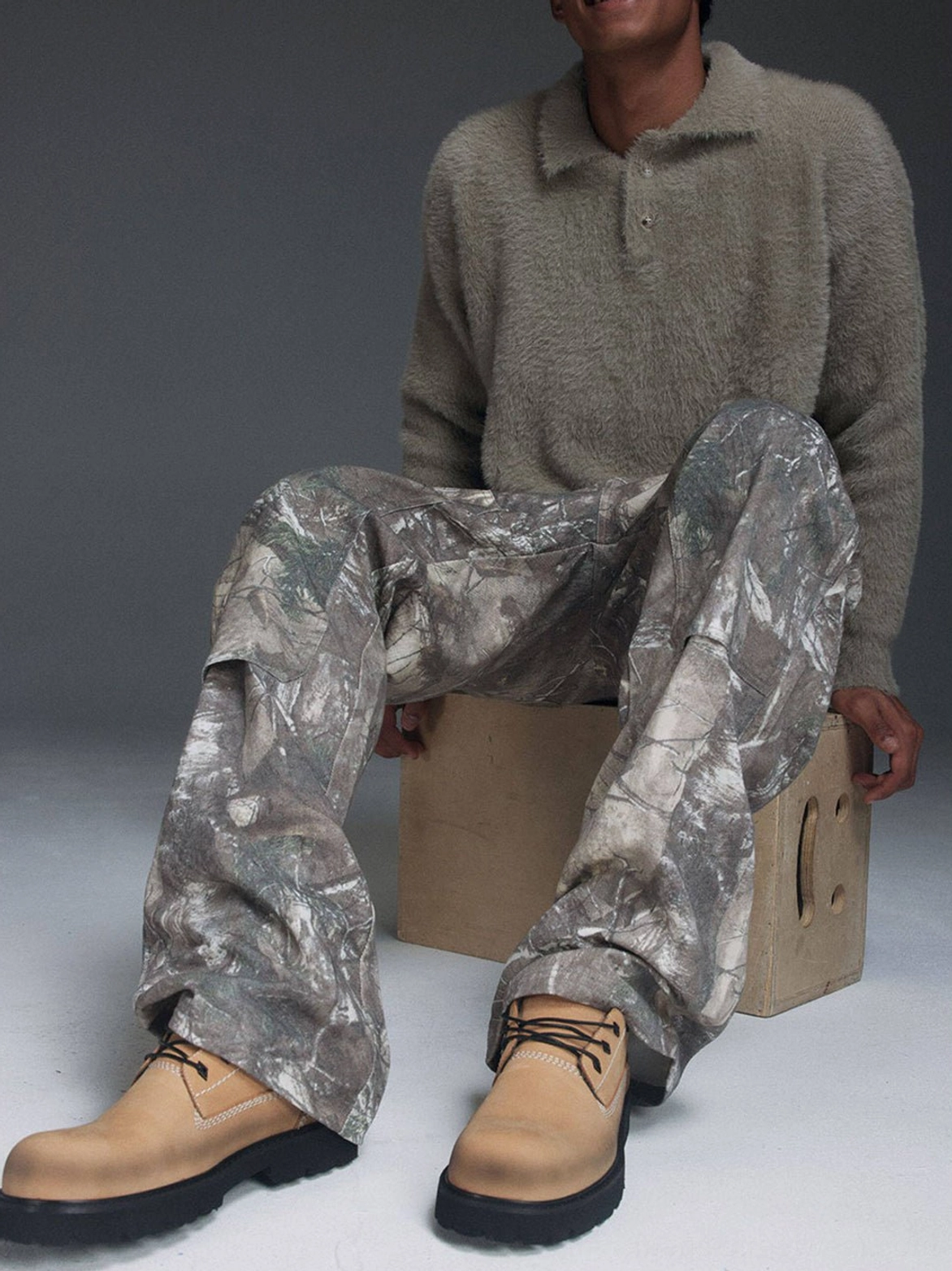Front view of tan leather lace-up lug-sole shoes styled with a casual taupe sweater and camouflage trousers