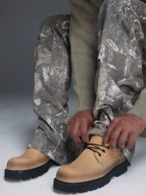 Model tying tan leather lug-sole lace-up shoes with black rugged outsole in a Korean streetwear outfit