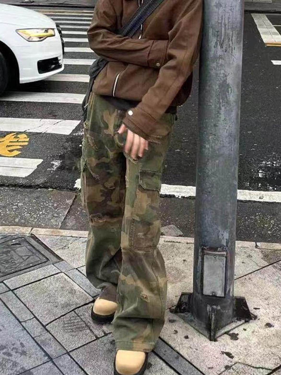 Tan leather lug-sole streetwear shoes worn with cropped jacket and camouflage cargo pants at an urban crosswalk