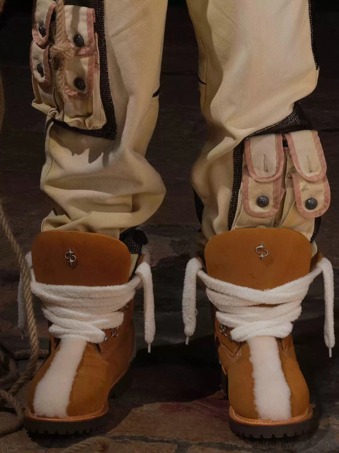 Model wearing tan shearling-lined work boots with utility cargo pants in an urban indoor streetwear outfit rear view