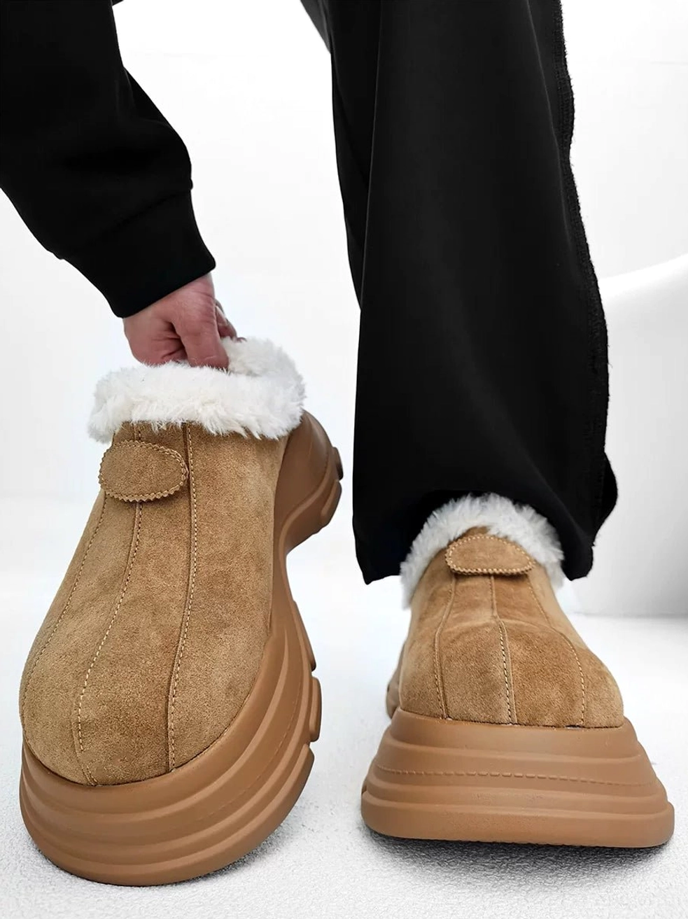 Tan suede-finish fleece platform clog held in hand with fluffy fur collar, round toe, chunky sole, and streetwear winter design