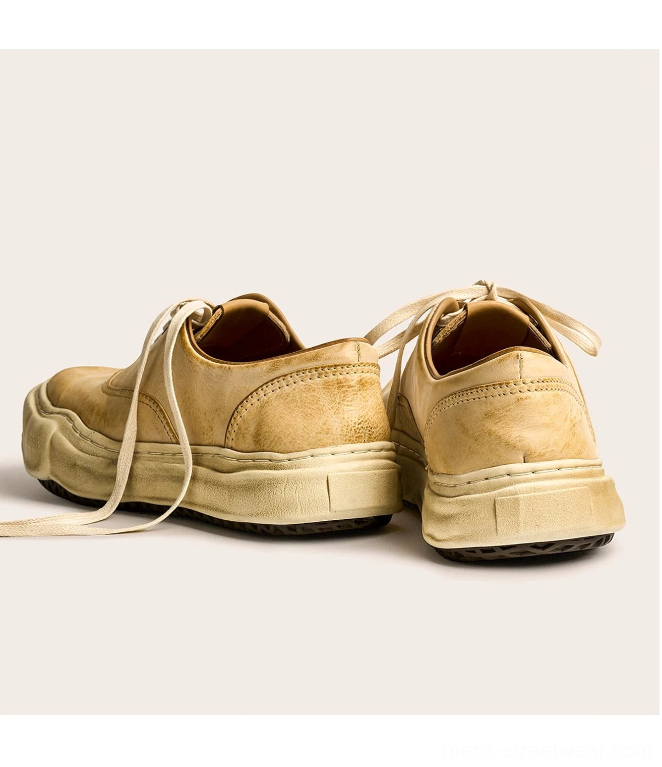 Rear three-quarter view of tan washed leather retro sneakers with loose laces, exposed heel counters, and thick weathered dissolved soles
