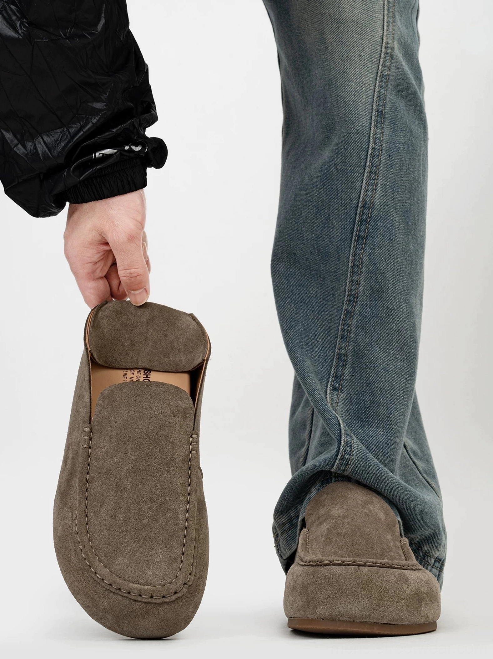 Taupe suede loafers held by the vamp showing soft leather texture, clean stitch lines, and foldable heel counter