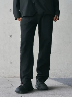 Black tech crinkled track pants front low angle view with relaxed straight leg fit and ankle zippers in minimalist urban streetwear setting