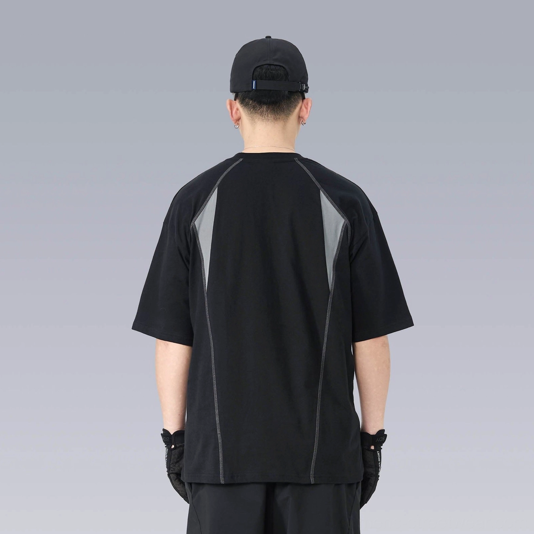 Back view of a loose techwear streetwear T-shirt showing the contrasting grey upper back panel, drop shoulders, and exposed seam details