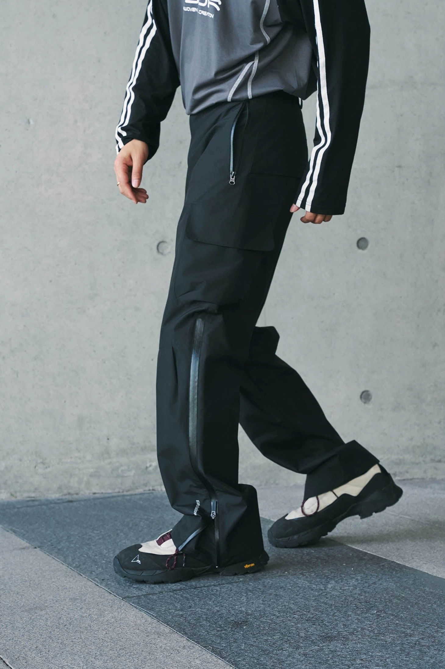 Techwear waterproof cargo pants shown in a dynamic side lower-body view with smooth fabric, ankle zipper, and hiking sneakers