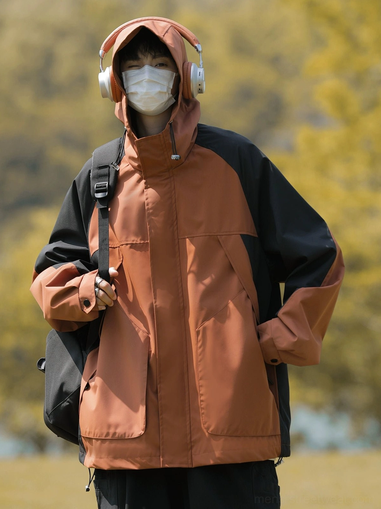 Male model wearing a terracotta orange and black colorblock outdoor windbreaker jacket with oversized pockets