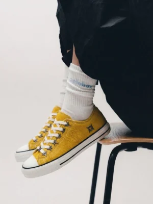 Mustard yellow textured cowhide low-profile sneakers worn with white socks and loose black pants overhead on-foot view