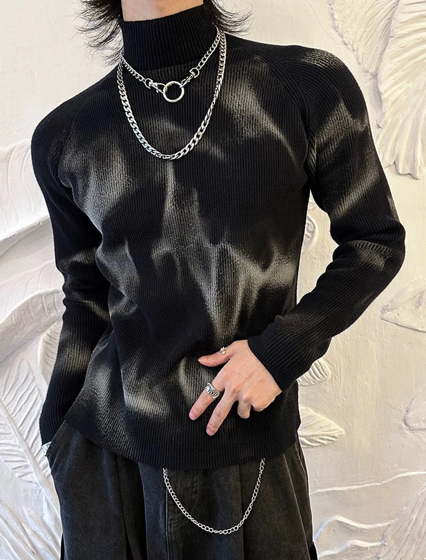 Three-quarter view of slim black tie-dye ribbed turtleneck sweater styled with silver necklaces and a waist chain