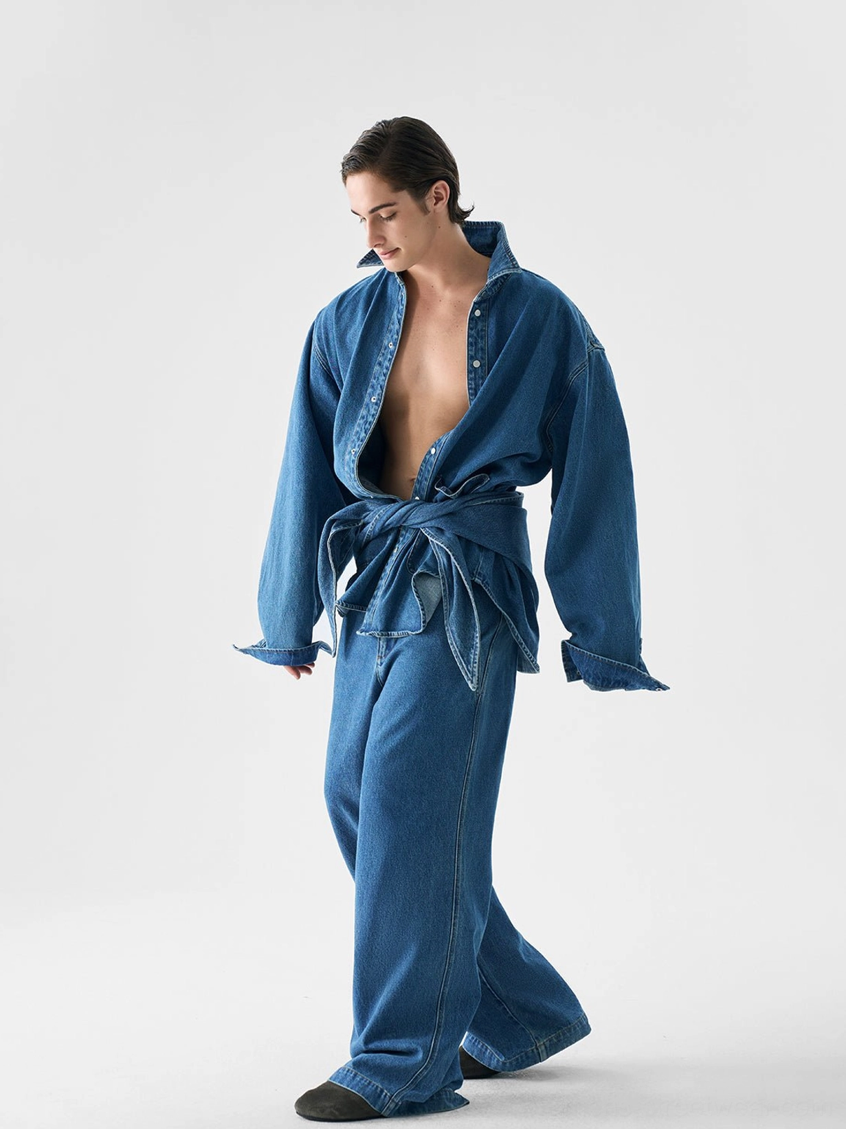 Side three-quarter view of a tie-front oversized denim jacket and relaxed wide-leg pants outfit in indigo blue