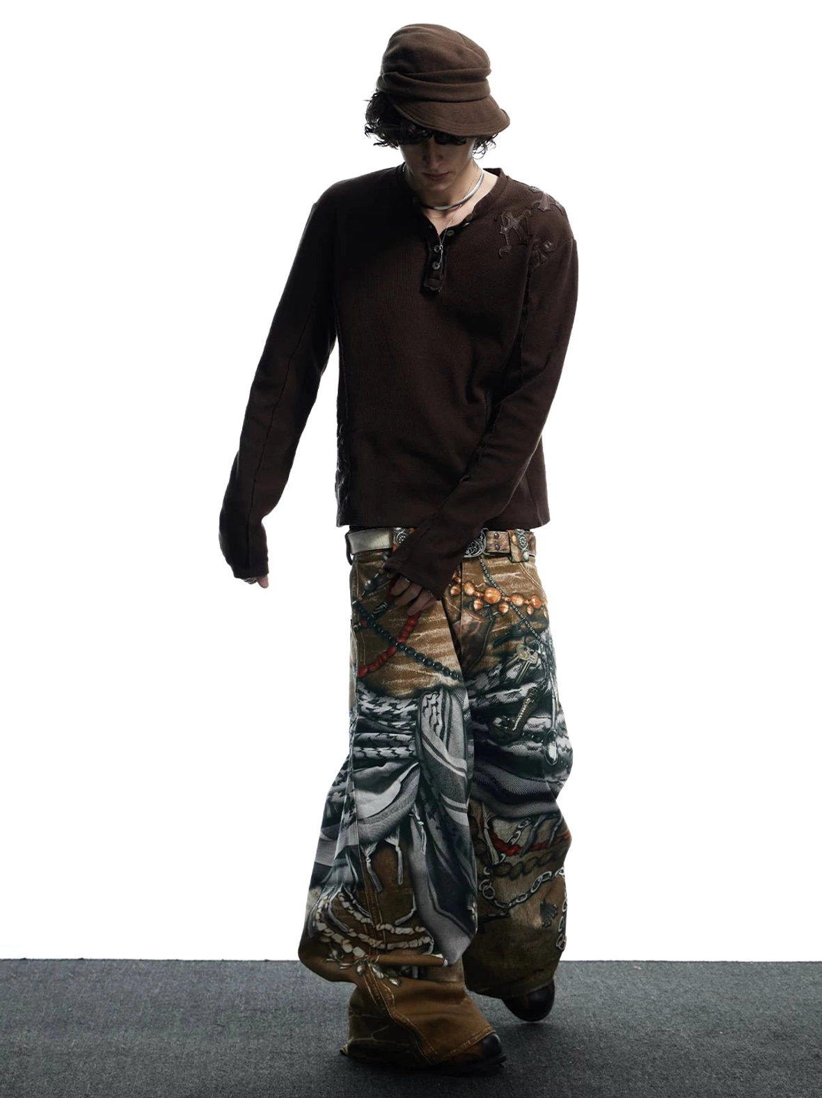 Full-body side view of tribal collage graphic wide-leg jeans with complete all-over vintage prints styled with a brown bucket hat and dark henley top
