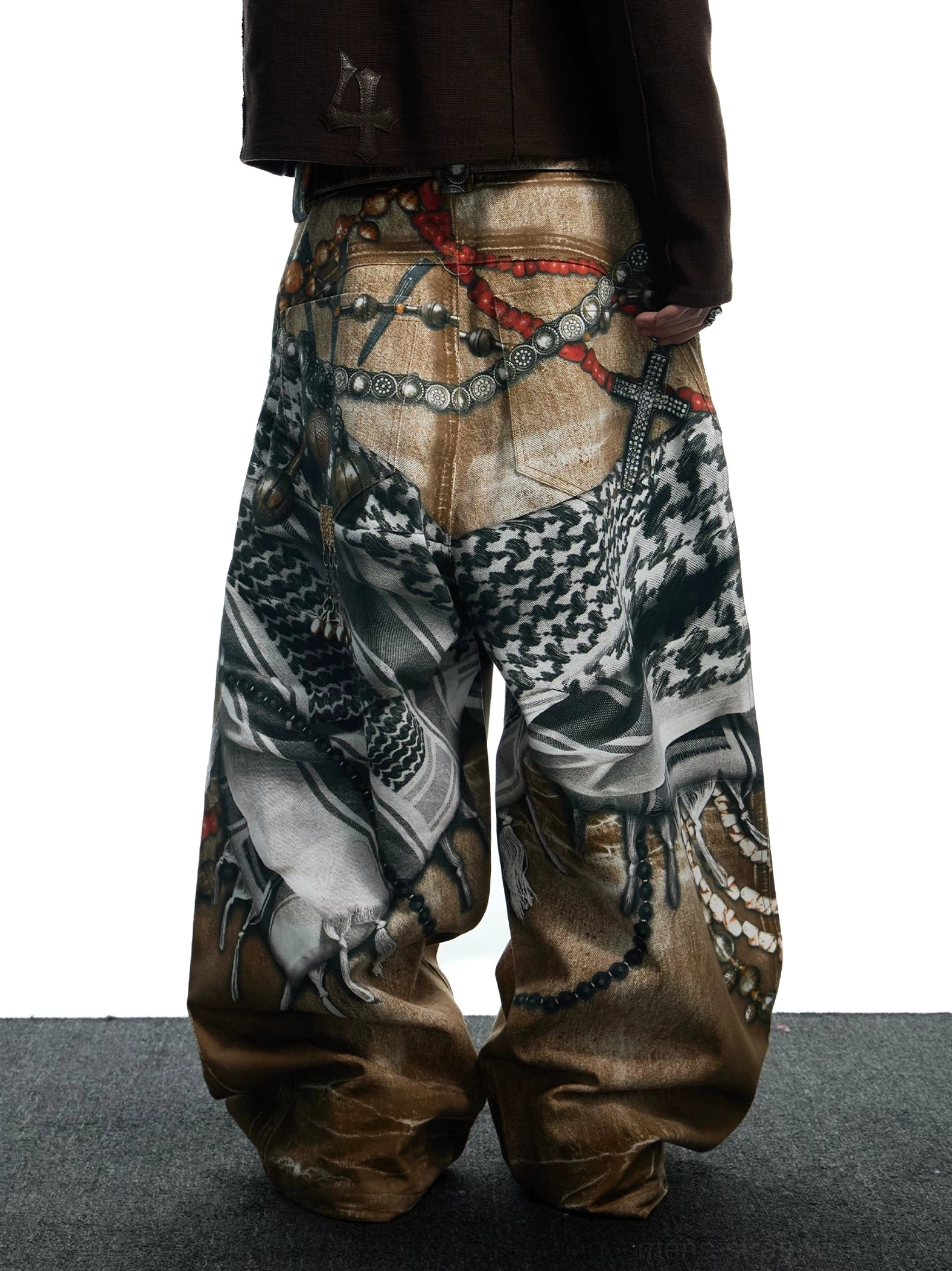 Rear low-angle view of relaxed tribal collage wide-leg jeans showing detailed chain bead and ornamental graphic prints across the back panels