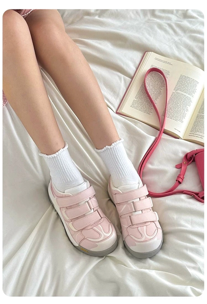 Pink adjustable strap platform sneakers arranged with white socks, an open book, and a handbag