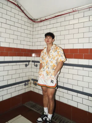 Full-body view of a male model wearing an oversized tropical floral shirt styled with white athletic shorts and streetwear sneakers