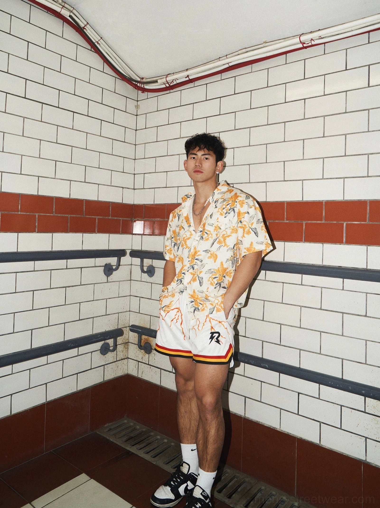 Full-body view of a male model wearing an oversized tropical floral shirt styled with white athletic shorts and streetwear sneakers