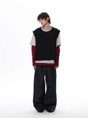 Rear view of a male model wearing a black beige and burgundy two-tone layered vest tee top with wide-leg dark denim in a minimalist streetwear studio