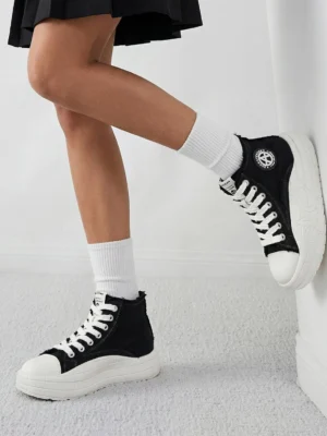 Black and white platform high-top canvas sneakers styled with white crew socks and a black pleated skirt