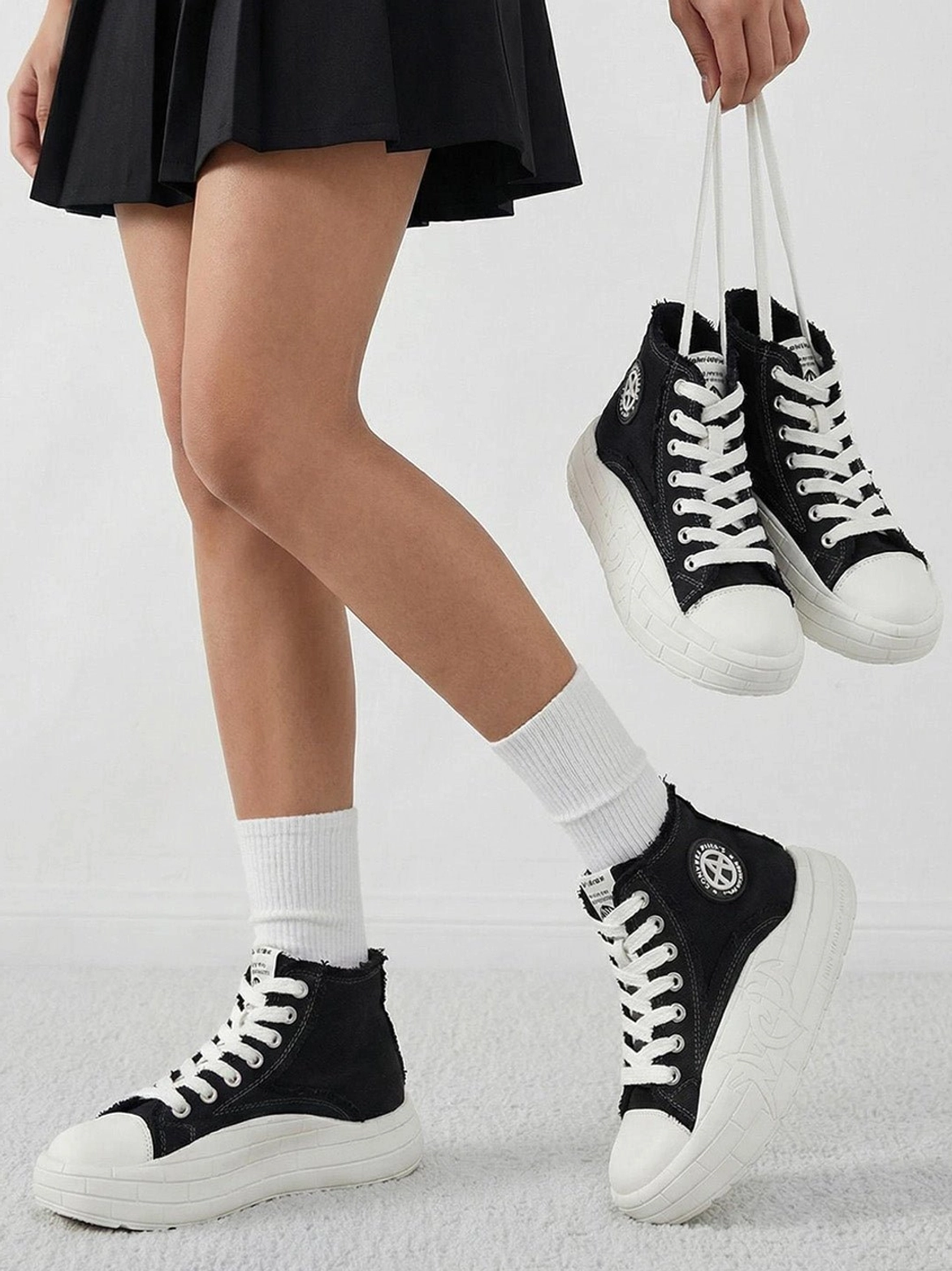 Black and white canvas platform high-tops shown with a pleated skirt outfit in a streetwear styling shot
