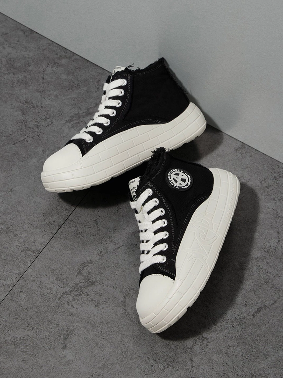 Diagonal view of black and white high-top platform sneakers with contrast panels, laces, and side badge