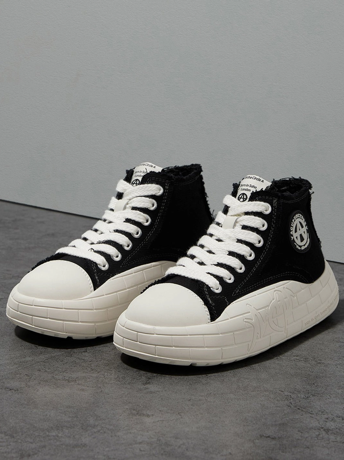 Pair of black and white two-tone canvas platform high-tops shown from the side on a dark floor