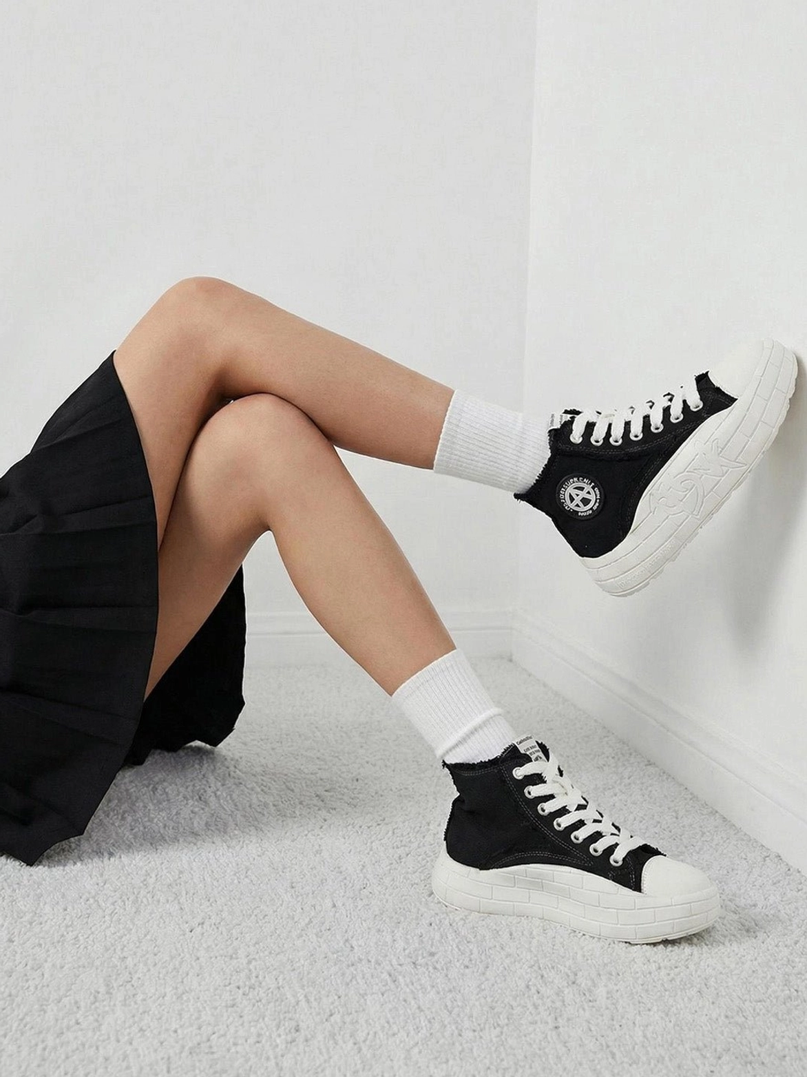 Black and white high-top platform sneakers worn with white socks and a black pleated skirt