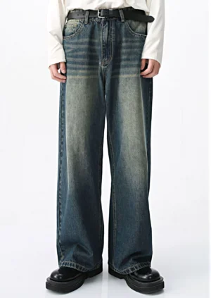 Front full-body view of mid-blue two-tone vintage wash wide-leg streetwear jeans styled with a white long-sleeve top, black belt, and chunky black leather shoes