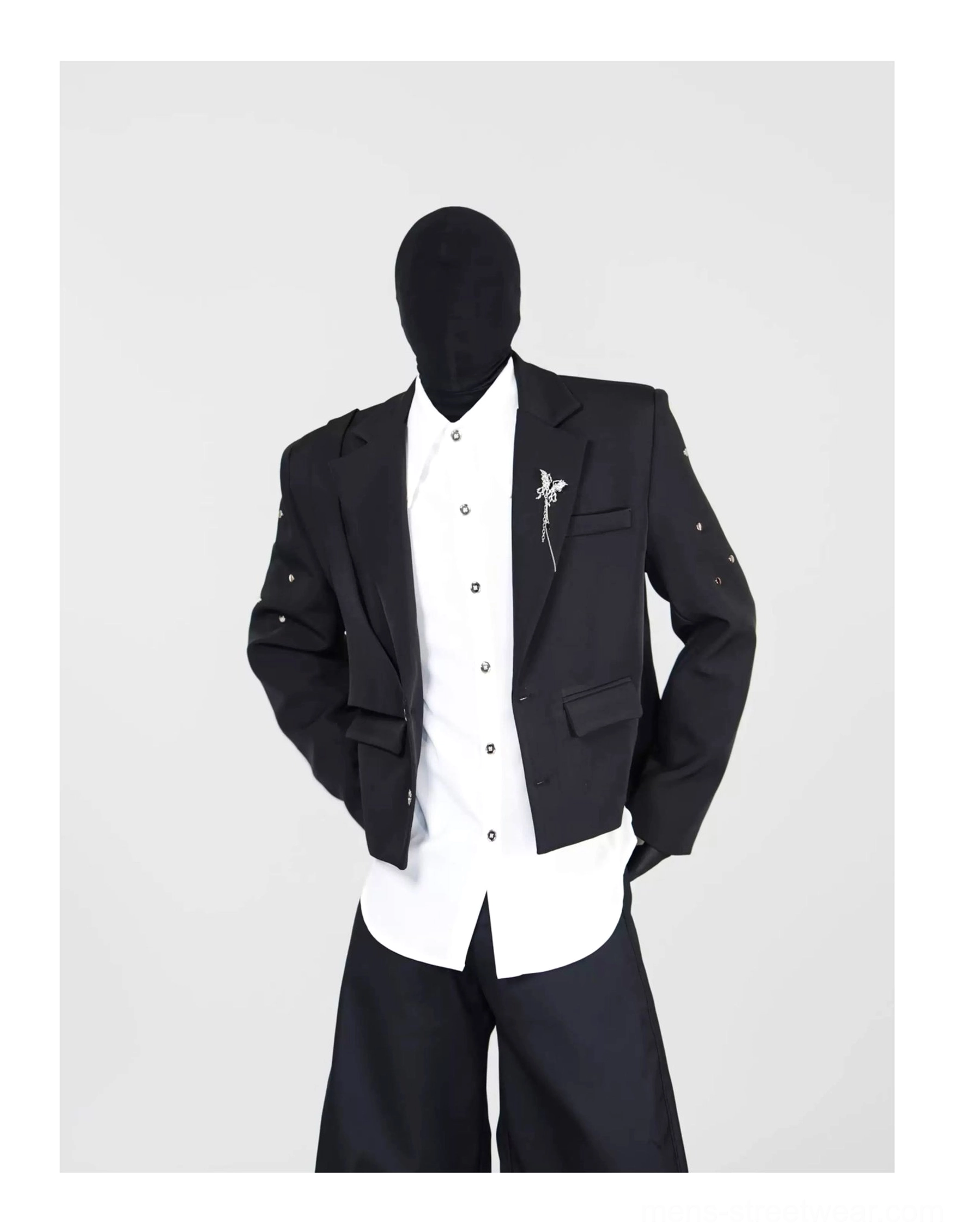 Three-quarter front view of an unbuttoned black cropped blazer layered over a white shirt with decorative brooch and wide-leg trousers