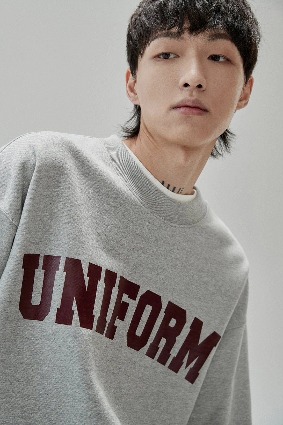 Close-up front view of UNIFORM collegiate lettering on a vintage-inspired gray cotton crewneck sweatshirt