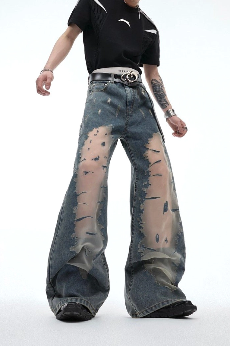 Front angled view of unisex blue streetwear jeans with mesh thigh panels, relaxed wide leg fit, distressed detailing, and leather belt styling
